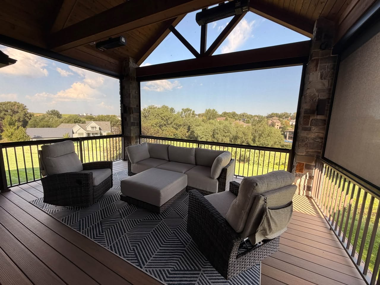 Covered deck with a vaulted wood ceiling, stone columns, and outdoor seating beside a motorized retractable screen